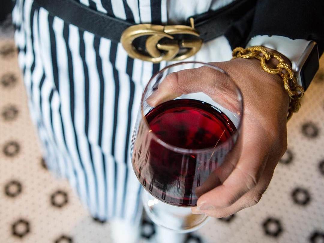 Woman holding a red glass of wine in a black-and-white outfit that matches the tile floor at Prost Wine Bar & Charcuterie in Frankenmuth