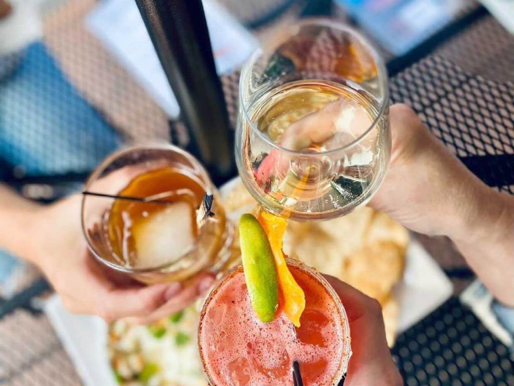 Three people sharing in a cheers with their drinks on the outdoor patio at Prost Wine Bar & Charcuterie in Frankenmuth