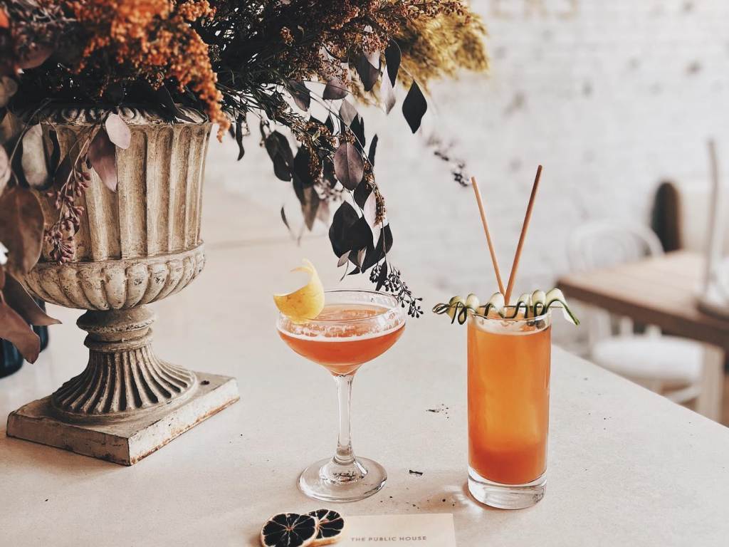 Two handcrafted house cocktails sitting on the bartop at The Public House in Bay City next to a beautiful dried floral arrangement
