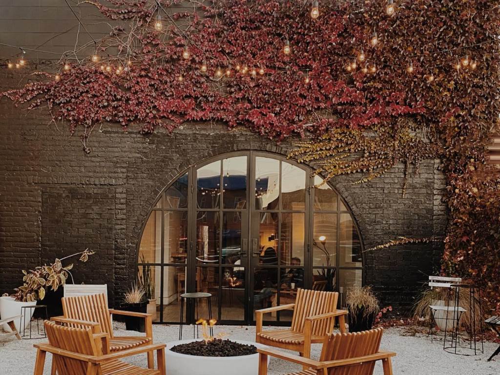 Cozy fall views of the patio at Harless + Hugh Coffee in Bay City, with fire pit surround seating, overhead string lights, and rich, red ivy climbing up the brick building