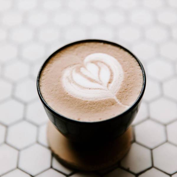 Heart-shaped latte art in a beautiful latte sitting on hexagon tile at Harless + Hugh Coffee in Bay City