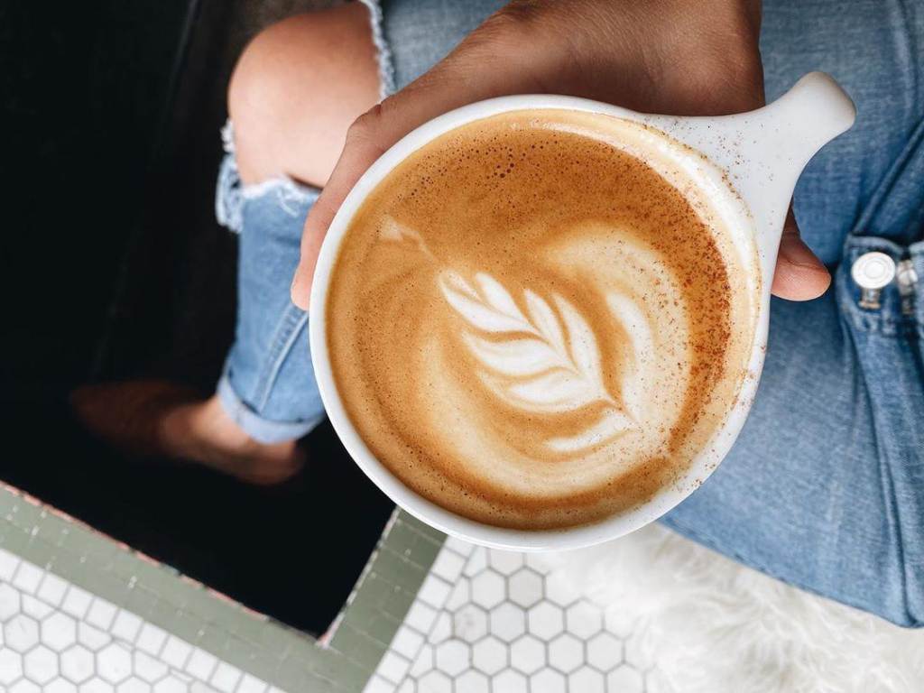 Woman holding a Pumpkin Spiced Latte with beautiful latte art at Harless + Hugh Coffee in Bay City