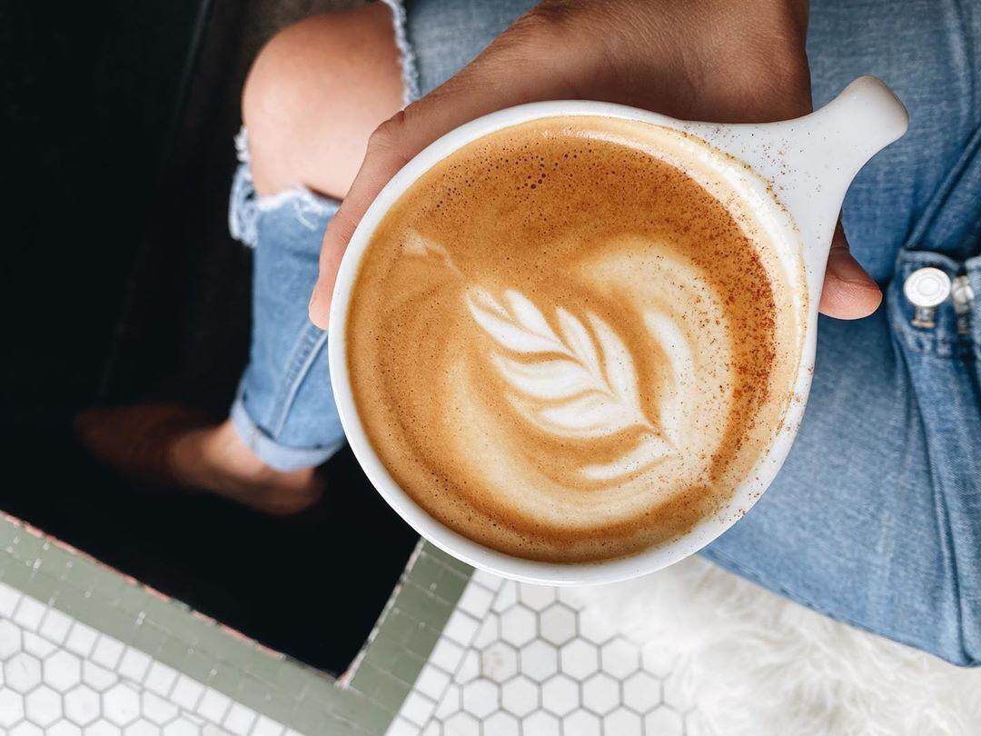 Woman holding a Pumpkin Spiced Latte with beautiful latte art at Harless + Hugh Coffee in Bay City