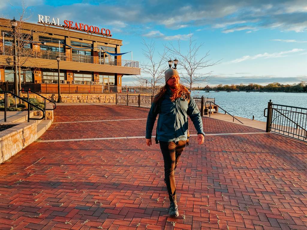 Guy walking away from Real Seafood Company in Uptown Bay City with the restaurant and riverfront in the background