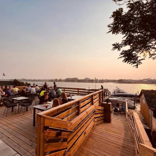 Soft sunset views of the multi-tiered waterfront dining deck leading down to the docks at Drift Shoreside Beer Garden along the Saginaw River in Downtown Bay City