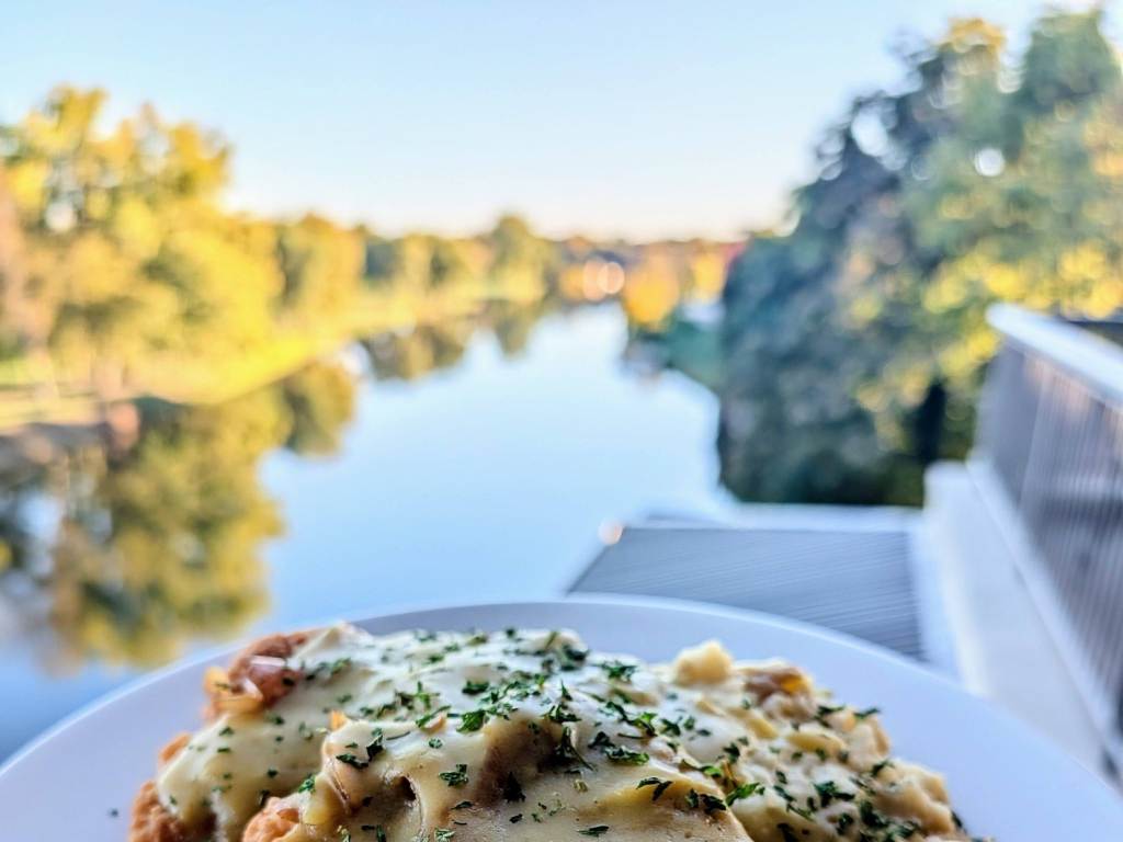 A beautiful plate of Schnitzel on the back deck of Frankenmuth Brewery in Frankenmuth, Michigan with scenic fall views of the Cass River in the background.