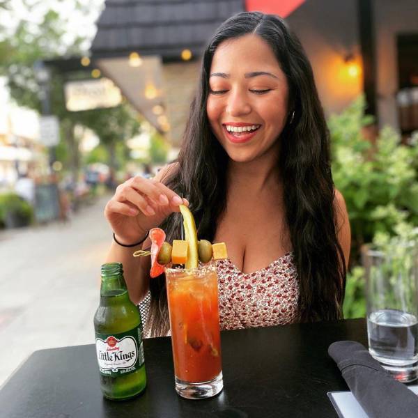 Woman smiling and getting ready to sample a Bloody Mary outside of Prost Wine Bar & Charcuterie