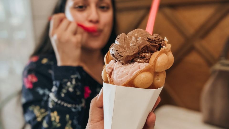Woman enjoying a bubble waffle cone at Cream & Sugar Ice Cream Company in Uptown Bay City