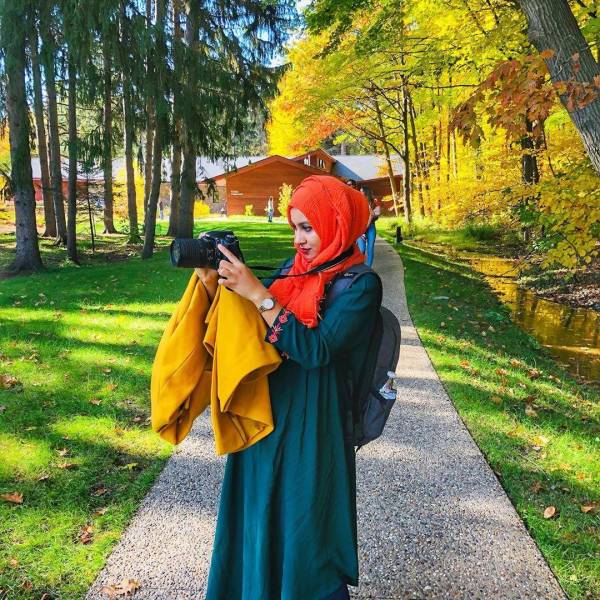 Woman in colorful clothing taking fall color pictures with her camera on the ground trails at Whiting Forest of Dow Gardens in Midland