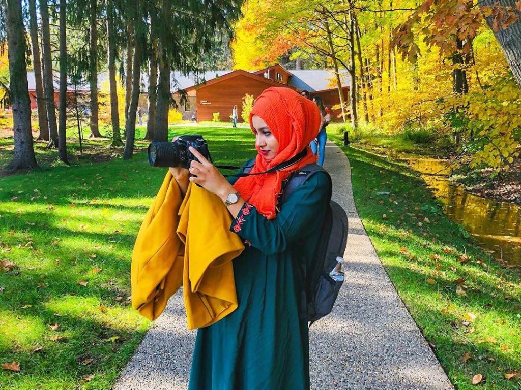 Woman in colorful clothing taking fall color pictures with her camera on the ground trails at Whiting Forest of Dow Gardens in Midland