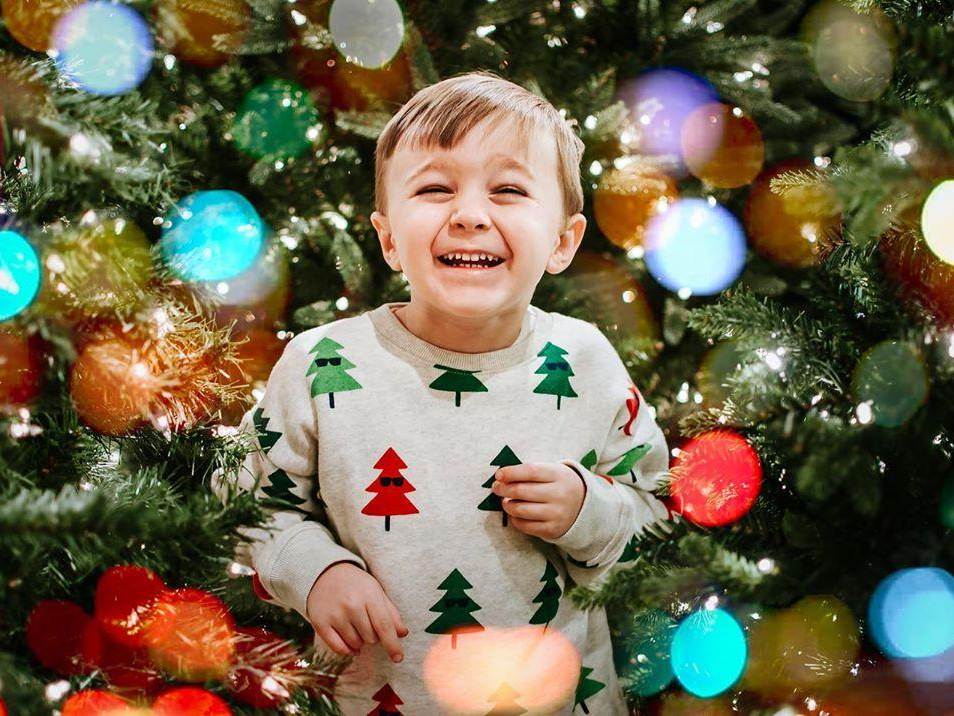 Little boy laughing and smiling, surrounded by Christmas trees and holiday lights, while he enjoys the world's largest Christmas store at Bronner's CHRISTmas Wonderland in Frankenmuth