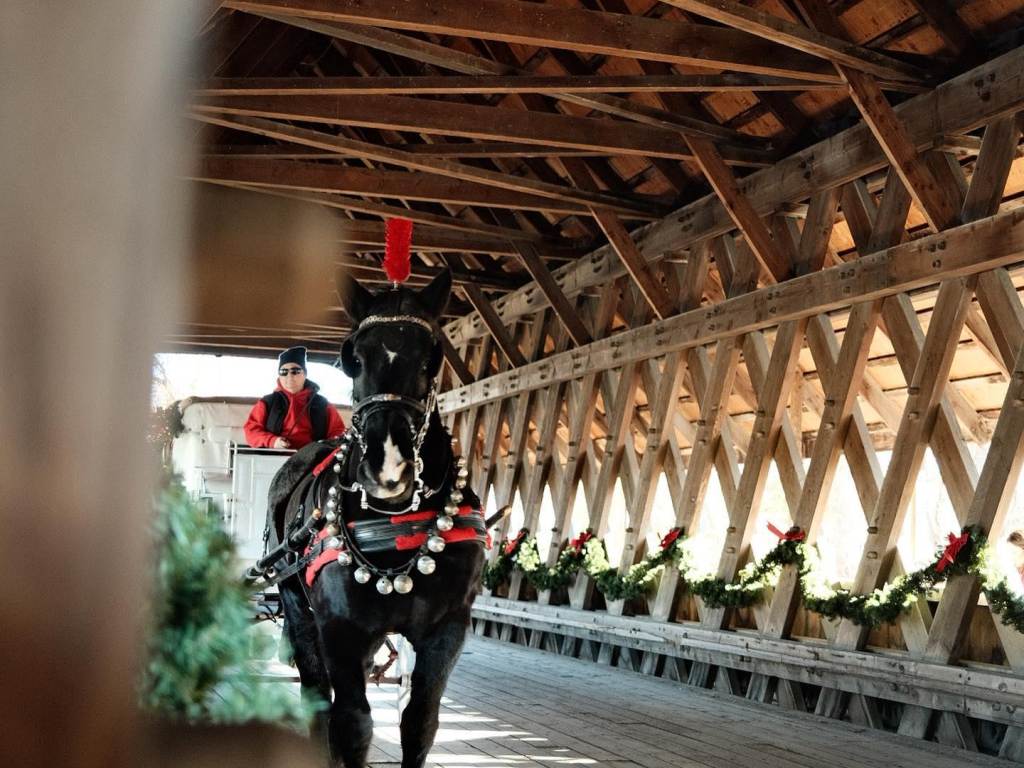 A beautiful, festive horse-drawn carriage from Fantasy Carriage Company, crossing the decorated Bavarian Inn Holz Brucke (covered wooden bridge) in Downtown Frankenmuth