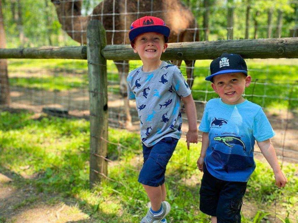 Two young boys smiling in front of a camel at Wilderness Trails Zoo in Birch Run