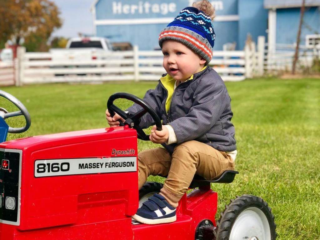 Little boy on a miniature red tractor at Grandpa Tiny's Farm in Frankenmuth, with a big, blue barn in the background