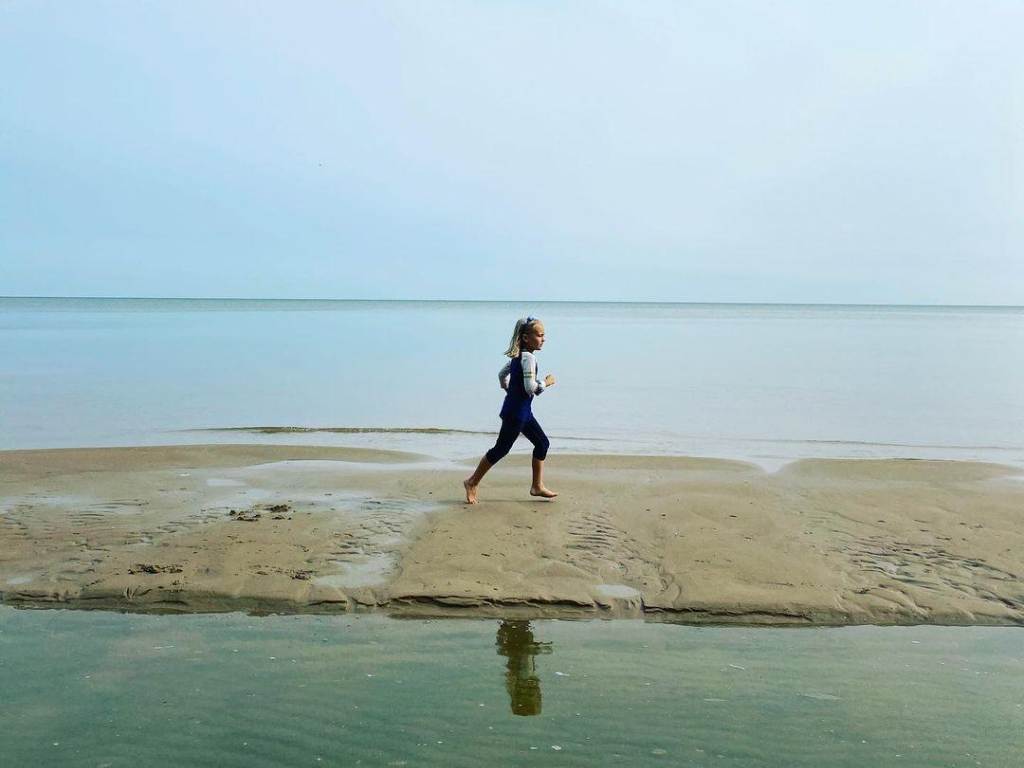 Little girl running on the sandy beachfront at Bay City State Park in Bay City