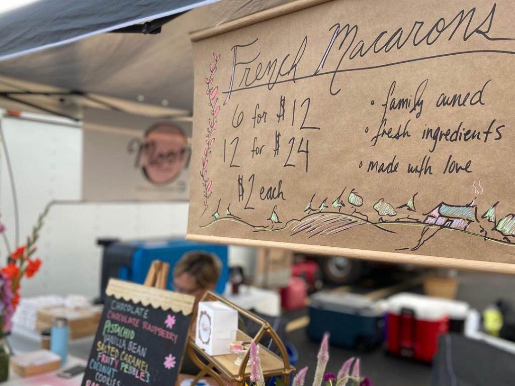 Handwritten sign advertising French macarons hanging over the Moon Macarons stand at the Midland Area Farmers Market in Midland