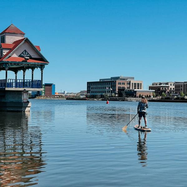 Guy on a stand-up paddleboard passing by the Riverwalk Pier on the Saginaw River in Bay City