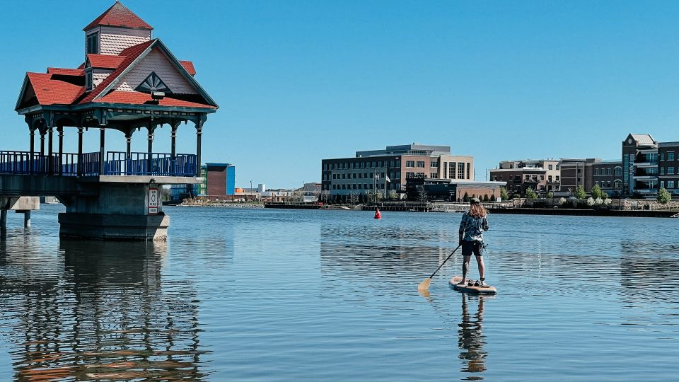 Guy on a stand-up paddleboard passing by the Riverwalk Pier on the Saginaw River in Bay City