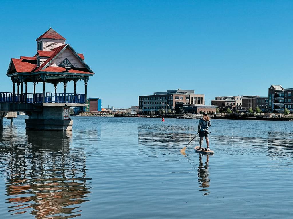Guy on a stand-up paddleboard passing by the Riverwalk Pier on the Saginaw River in Bay City