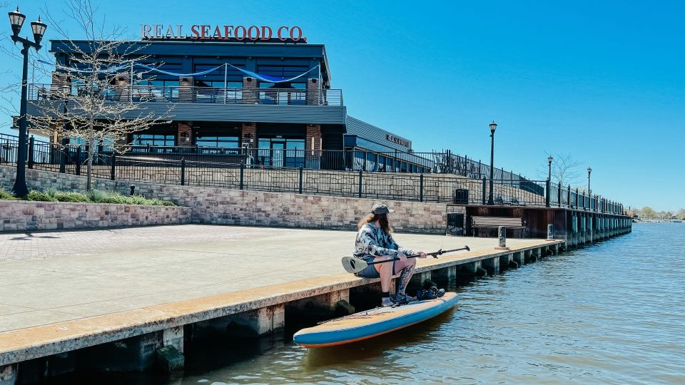 Guy sitting along the Saginaw River in Bay City with his stand-up paddleboard by Real Seafood Company in Uptown